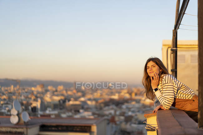 Ritratto di contenuto giovane donna che si rilassa sulla terrazza sul tetto al tramonto — Foto stock