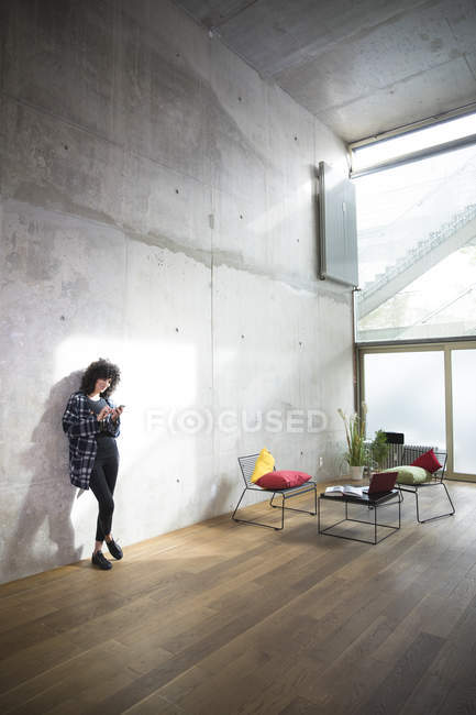 Woman leaning against concrete wall in a loft using cell phone — Stock Photo