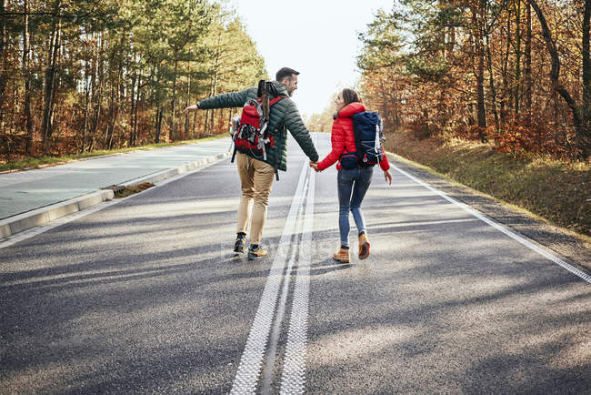 Счастливая пара, идущая посреди пустой дороги в хорошем настроении — стоковое фото