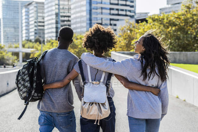 Tre amici che esplorano la città, camminano per strada, a braccetto — Foto stock