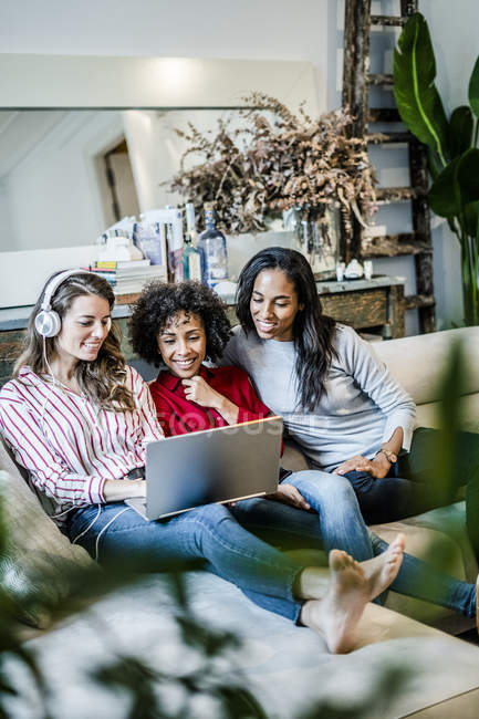 Drei glückliche Frauen mit Laptop sitzen auf der Couch — Stockfoto