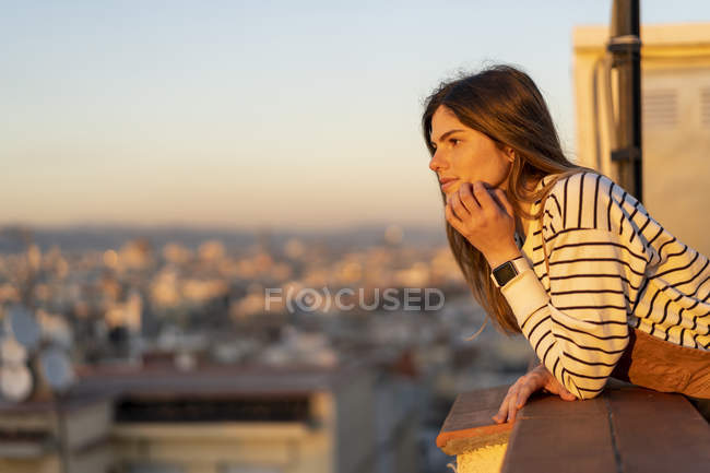 Jeune femme se relaxant sur le toit terrasse au coucher du soleil — Photo de stock