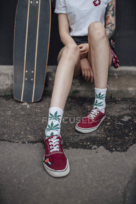 Image recadrée de la femme en chaussettes et baskets assis à côté de skateboard sculpteur — Photo de stock