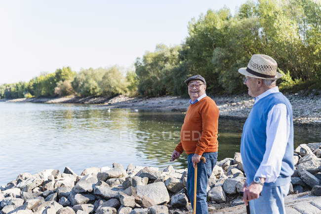 Dois velhos amigos em pé perto do lago, a partilhar memórias — Fotografia de Stock