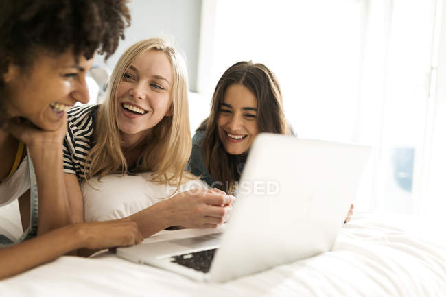 Trois jolies copines allongées sur un ordinateur portable partagé — Photo de stock