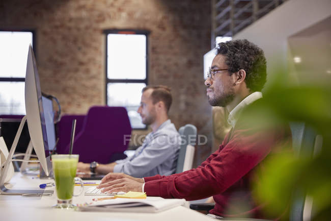 Giovane uomo seduto alla scrivania in ufficio, sorridente — Foto stock