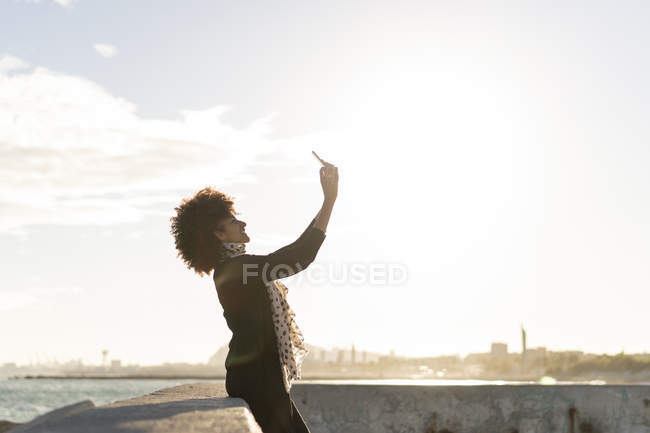 Smiling woman taking selfie with smartphone near the sea — Stock Photo