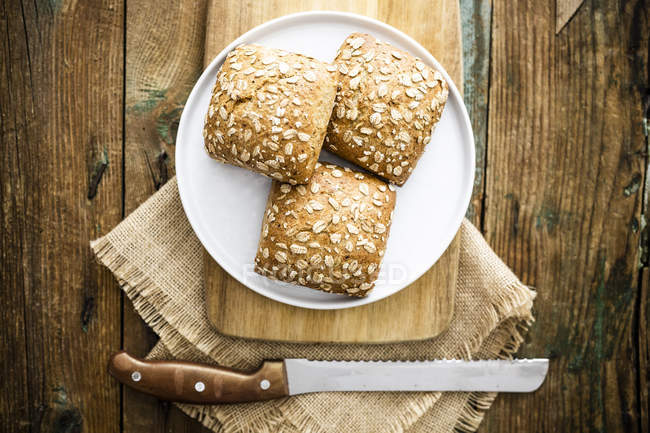 Three whole meal bread rolls with oat flakes on plate — Stock Photo