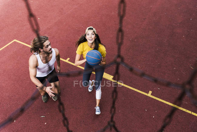 Joven hombre y mujer jugando baloncesto en el campo de baloncesto - foto de stock