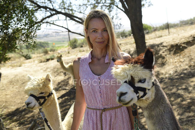 Porträt einer lächelnden blonden Frau mit zwei angeleinten Alpakas — Stockfoto