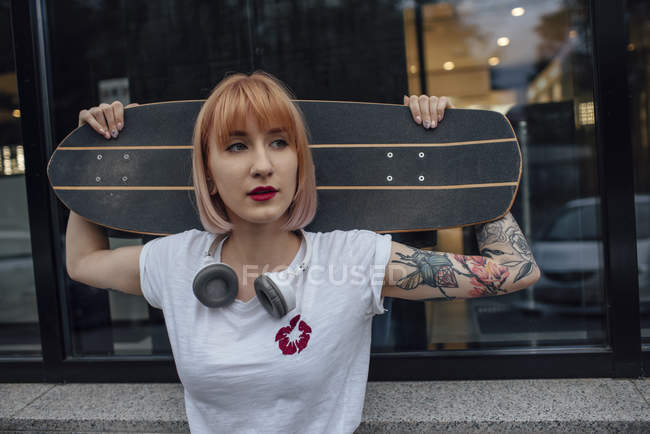 Joven mujer sosteniendo carver monopatín fuera de un edificio - foto de stock