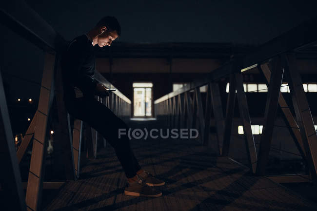 Sportive young man with smartphone and earphones standing on a bridge at night — Stock Photo