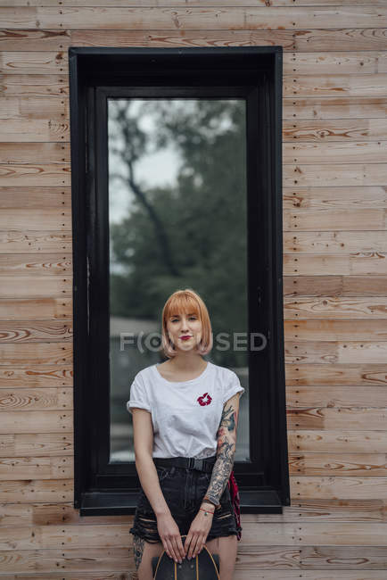 Retrato de mujer joven de pie fuera del edificio con monopatín tallador - foto de stock