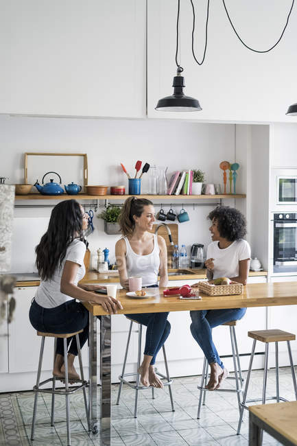 Tre donne felici sedute al tavolo della cucina a casa a socializzare — Foto stock