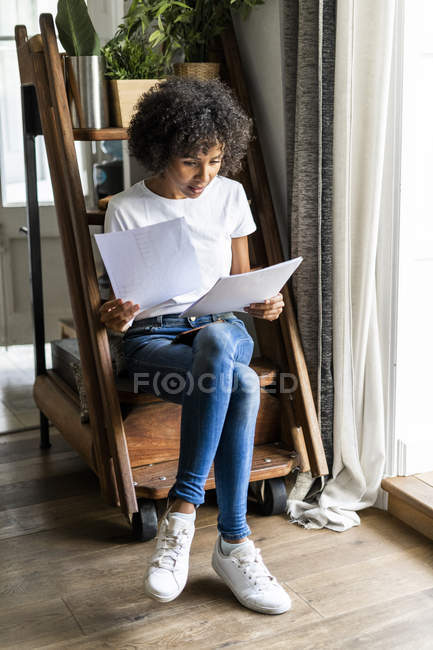 Mujer sentada en escalones en casa mirando el documento - foto de stock