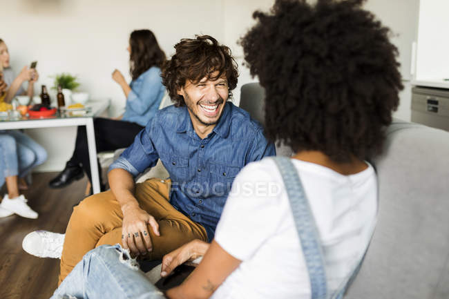 Felice coppia seduta su divano parlando con gli amici in background — Foto stock