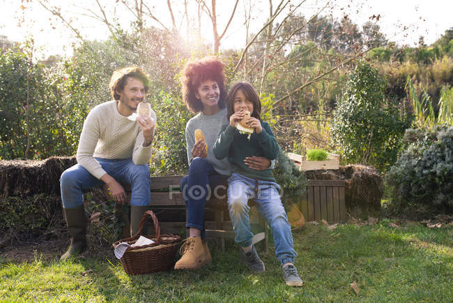 Famiglia felice seduta in giardino, prendersi una pausa, mangiare panini — Foto stock