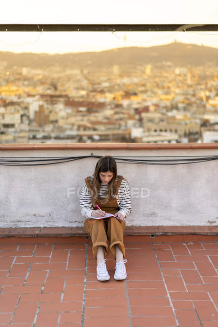 Giovane donna seduta sulla terrazza sul tetto prendere appunti — Foto stock