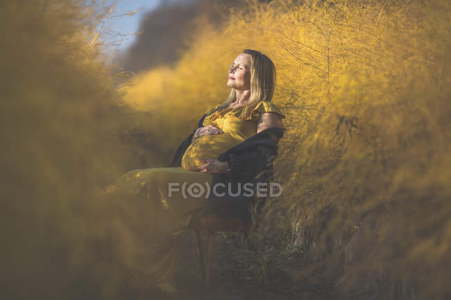 Pregnant woman sitting on chair in asparagus field in autumn — Stock Photo