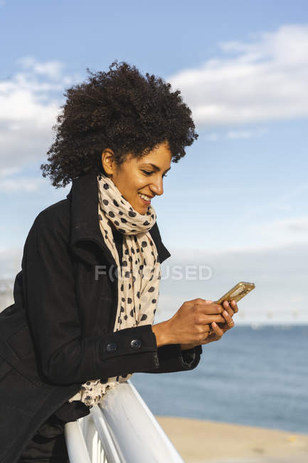 Посмішка жінка спирається на поручні дивлячись на мобільний телефон — стокове фото