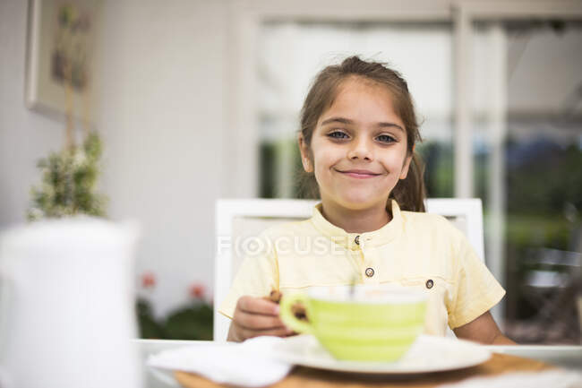 Portrait of smiling little girl having breakfast at home — Stock Photo