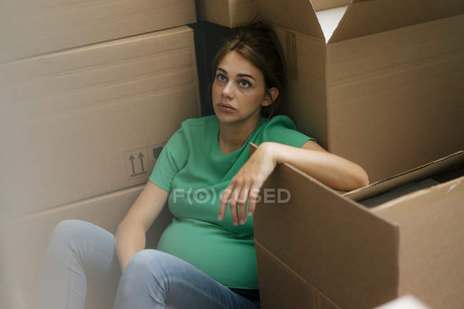 Mulher grávida exausta sentada no chão cercada por caixas de papelão — Fotografia de Stock