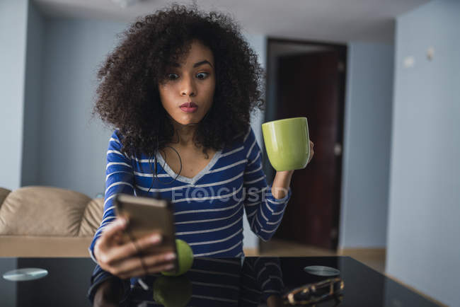 Portrait of young woman with mug starring at cell phone — Stock Photo