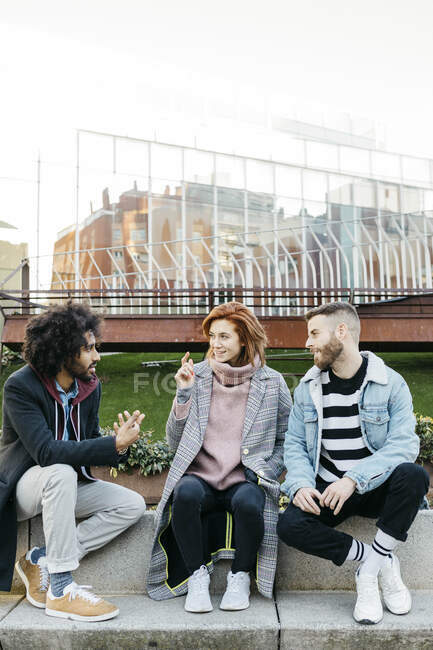 Três amigos sentados na cidade conversando — Fotografia de Stock