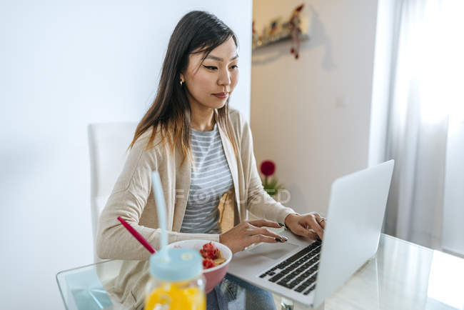Young woman eating breakfast, while working on laptop — Stock Photo