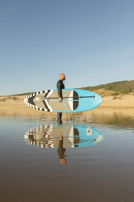 Spain, Andalusia, Tarifa, man holding stand up paddle board in the sea — Stock Photo