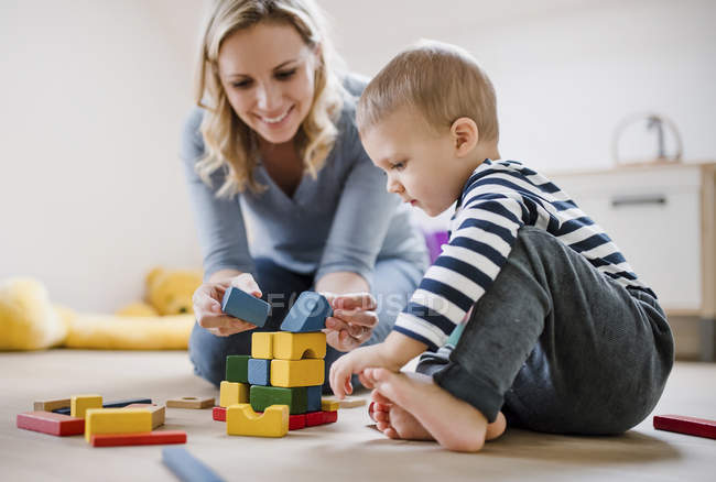 Sorridente madre e figlio bambino che gioca con i blocchi di costruzione a casa — Foto stock
