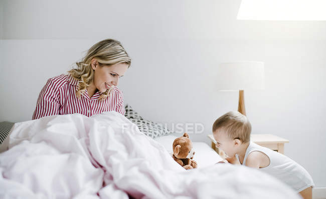 Sorridente madre che gioca con il figlio bambino a letto a casa — Foto stock