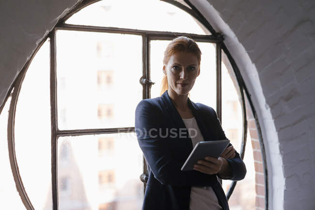 Portrait de femme d'affaires confiante avec tablette à la fenêtre — Photo de stock