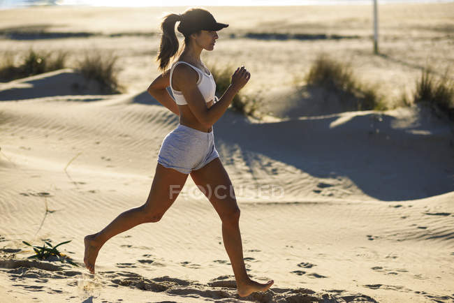 Sportive woman running along sand dunes on the beach — Stock Photo
