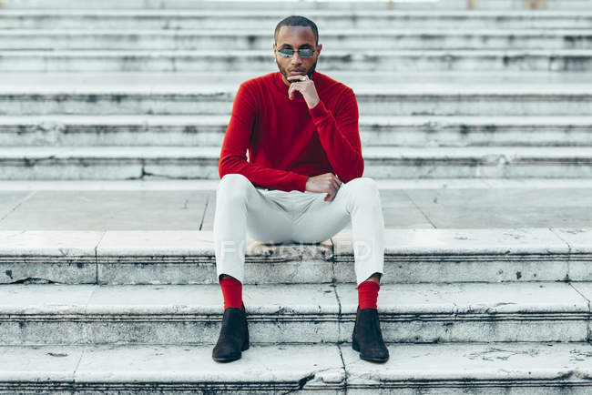 Портрет стильного молодого человека в красном свитере и носках, сидящих на лестнице — стоковое фото