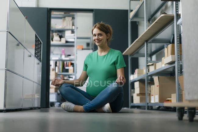 Smiling pregnant woman sitting on floor in office having a yoga break — Stock Photo