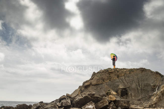 Donna con ombrello colorato in piedi su una collina sulla spiaggia — Foto stock