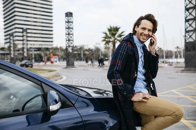 Spain, Barcelona, smiling man on cell phone outside car in the city — Stock Photo
