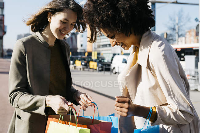 Deux femmes heureuses avec des sacs à provisions dans la ville vérifiant l'achat — Photo de stock