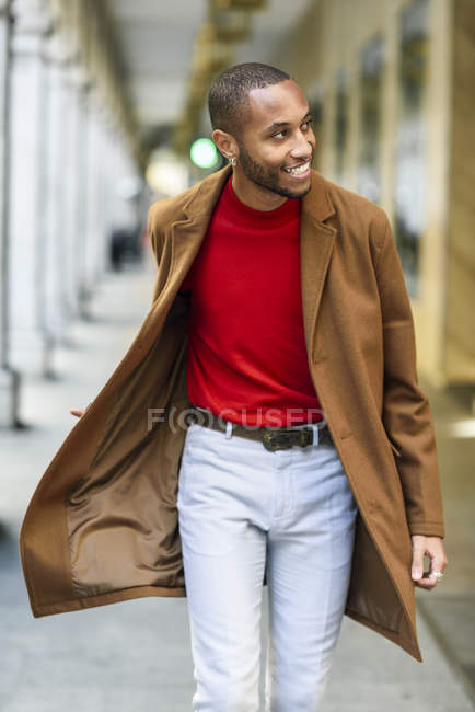 Modischer junger Mann mit rotem Pullover und braunem Mantel läuft an der Arkade entlang — Stockfoto