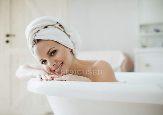 Retrato de una mujer sonriente con toalla alrededor de su cabeza tomando un baño en casa - foto de stock