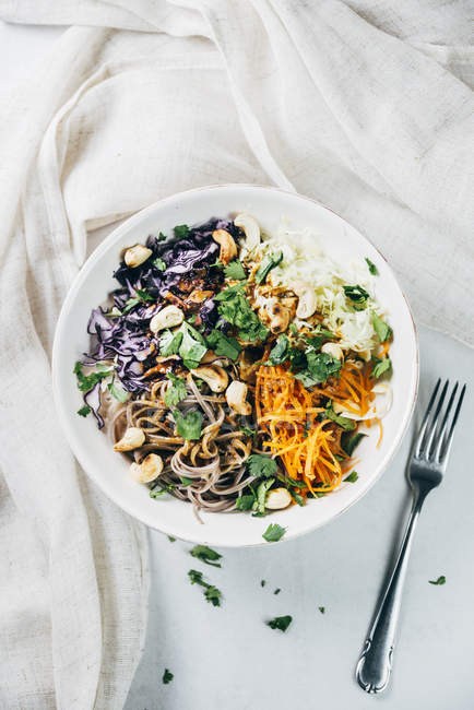 Bowl of buckwheat noodle salad with raw vegetables, roasted cashews,  coriander and spicy dressing — Stock Photo