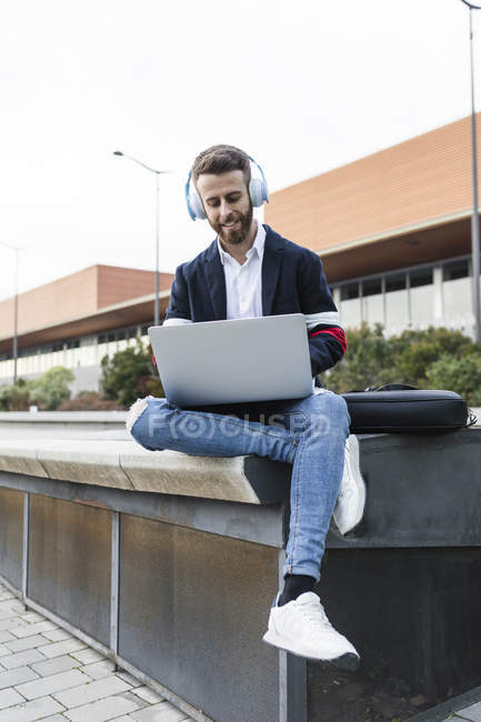 Стильний бізнесмен сидить у місті слухаючи музику і використовуючи ноутбук — стокове фото