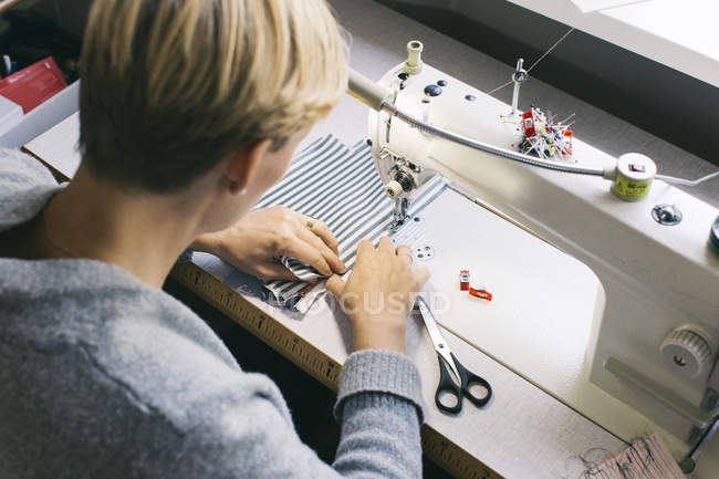Vista lateral de la modista mujer utilizando la máquina de coser en el estudio, fábrica de tela - foto de stock