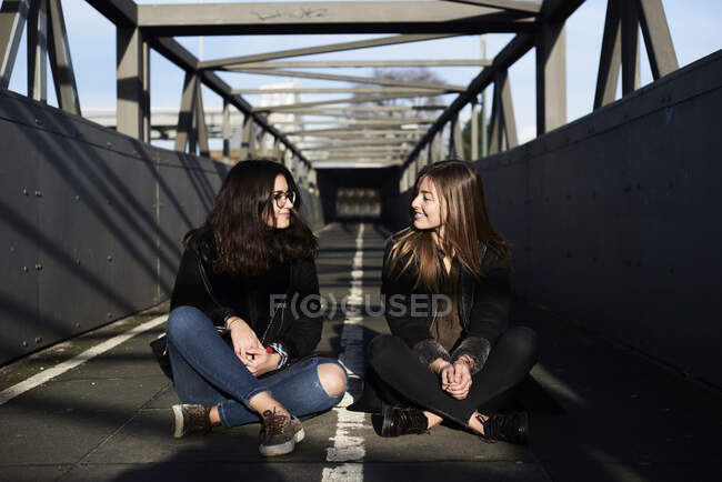 Dois amigos sentados numa ponte a olhar um para o outro — Fotografia de Stock