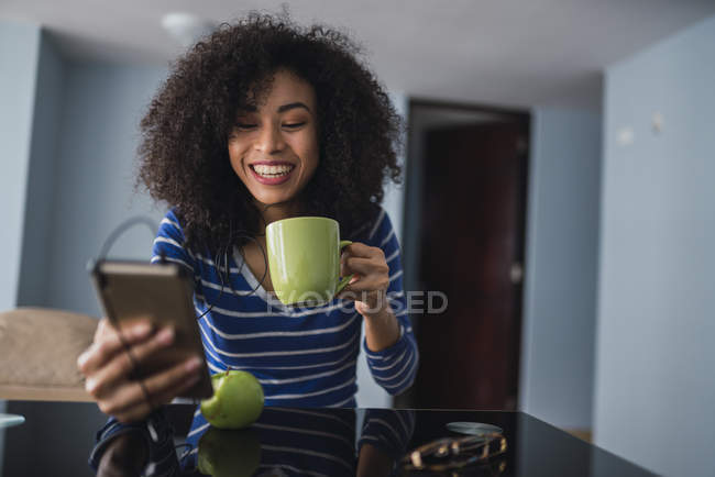 Портрет щасливої молодої жінки з чашкою кави, дивлячись на мобільний телефон. — стокове фото