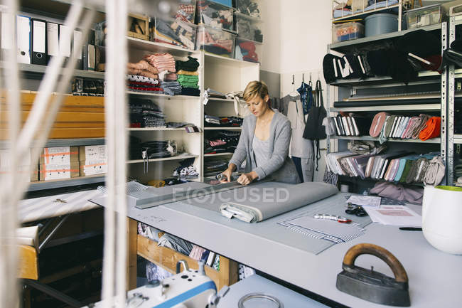 Caucasian woman fashion designer in atelier  working with grey fabric textile at table — Stock Photo