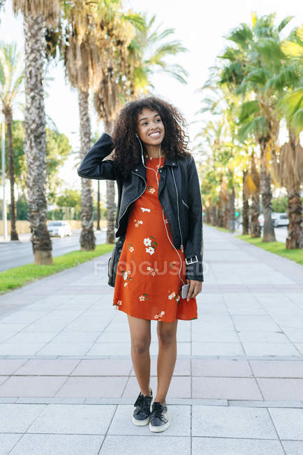 Portrait of smiling young woman on a promenade listening music with earphones and smartphone — Stock Photo