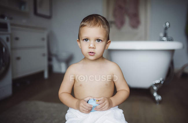 Ritratto di bambino che tiene in braccio un'anatra giocattolo in un bagno di casa — Foto stock