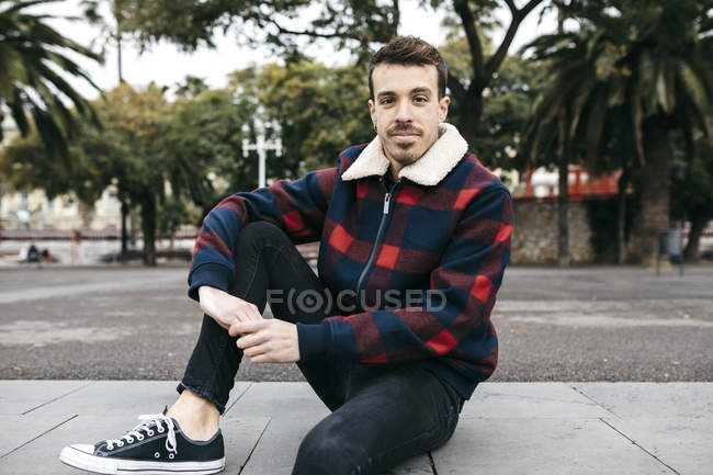 Joven vestido con ropa casual sentado en un banco de la ciudad - foto de stock